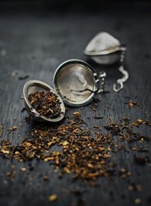 Close-up of loose black tea leaves in a metal tea infuser on a dark wooden surface