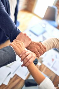 Four business people joining hands in a teamwork gesture.