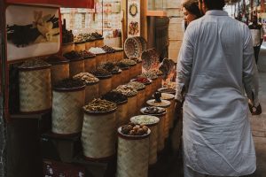 Customers browsing a variety of colorful spices displayed in large woven baskets at a traditional market stall.
